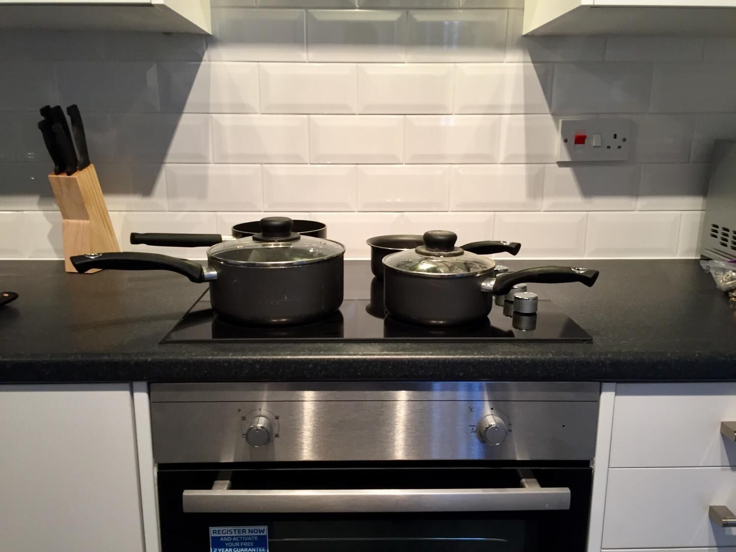 Een keuken met twee pannen op een fornuis, een messenblok en een roestvrijstalen oven.