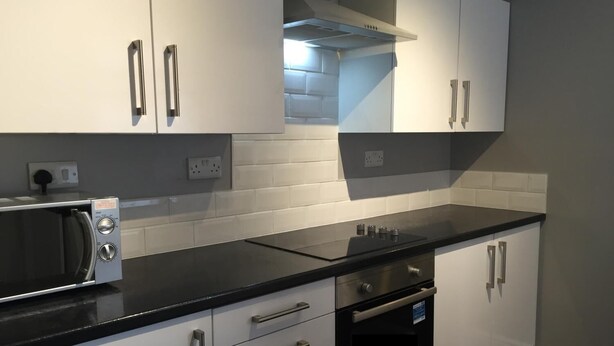 A modern kitchen with white cabinets, a black countertop, a built-in microwave, and an oven. - Samuel Place (Crewe)