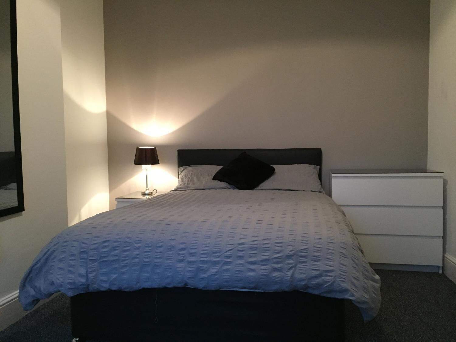 Een slaapkamer met een bed, nachtkastje met een lamp en een kledingkast.