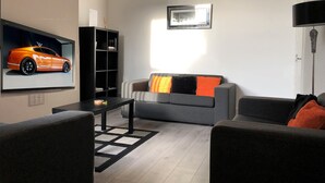 A modern living room with a grey sofa, black coffee table, and a black bookshelf. - Samuel Place (Crewe)