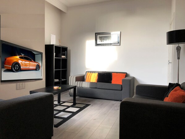 A modern living room with a grey sofa, black coffee table, and a black bookshelf.