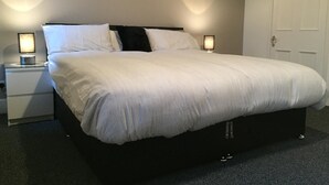 A neatly made bed with white bedding, two bedside tables with lamps, and a closed door in a hotel room. - Samuel Place (Crewe)