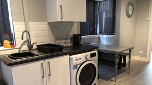 A compact kitchen with a washing machine, a sink, and a small table. - Samuel Place (Crewe)