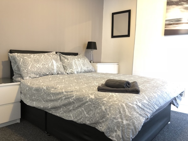 A neatly made bed with patterned bedding, a bedside lamp, and a framed picture on the wall.