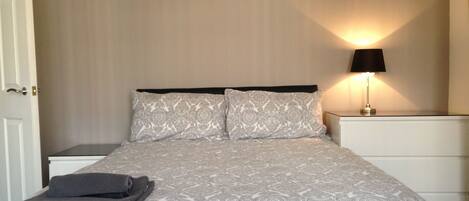 A neatly made bed with a patterned bedspread and pillows, a bedside lamp, and a folded towel on the nightstand.