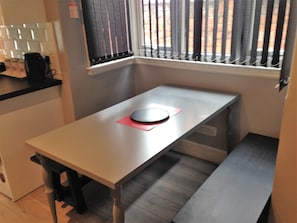 A small kitchen with a table, a bench, and a window with blinds.