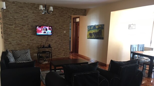 Ein Wohnzimmer mit Steinwand, einem Flachbildfernseher, einem Gemälde und einem Essbereich mit Tisch und Stühlen.