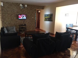 Un soggiorno con parete in pietra, televisore a schermo piatto, un quadro e un'area pranzo con tavolo e sedie.