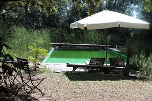 Una piscina con revestimiento verde, rodeada por un césped con bancos y una sombrilla.