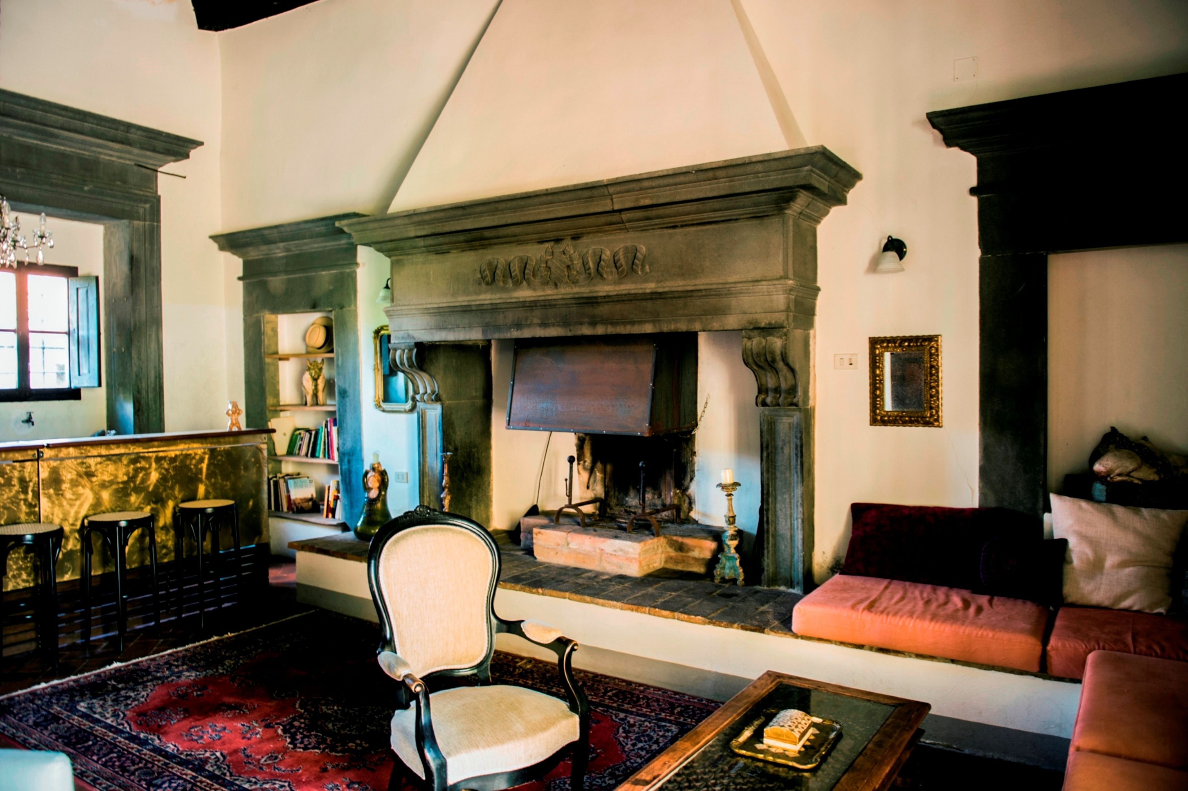 A traditional living room with a fireplace, a sofa, a chair, and a bar area with stools.