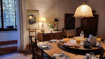 A dining area with a wooden table set for two, a hanging lamp, and a window with a view of trees.