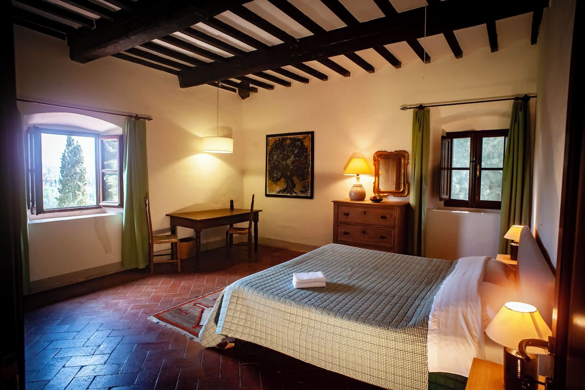A bedroom with a bed, a desk, a chair, a lamp, and a painting.