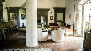 A spacious living room with a fireplace, a large marble column, and a view through an open door. - Il Poggio B&B (Scandicci)