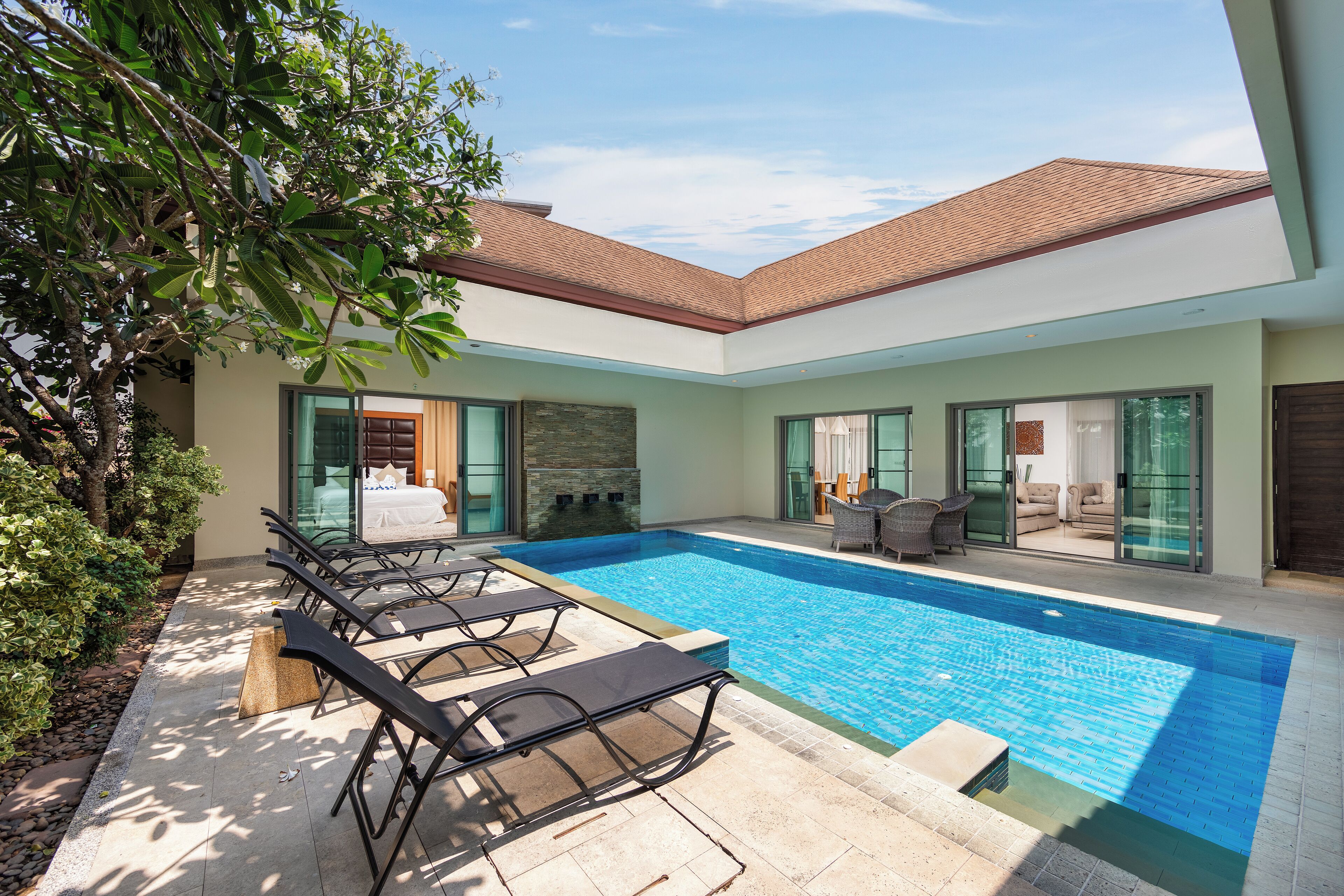 A modern pool area with lounge chairs, a stone wall, and a glass door leading to a living area.