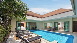 A modern pool area with lounge chairs, a stone wall, and a glass door leading to a living area.