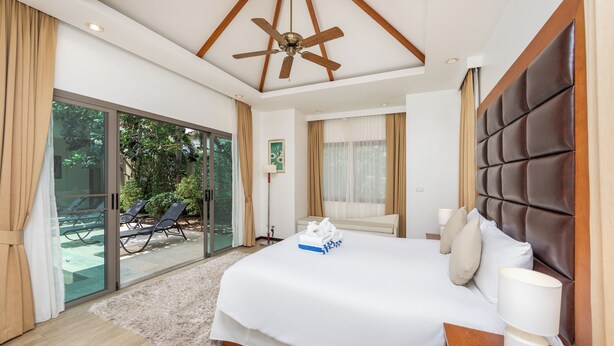 A spacious bedroom with a large bed, a ceiling fan, and a view of a garden through a sliding glass door.