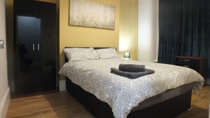 A bedroom with a large bed, a dark wardrobe, a painting on the wall, and a nightstand with a lamp. - Walthall Place (Crewe)