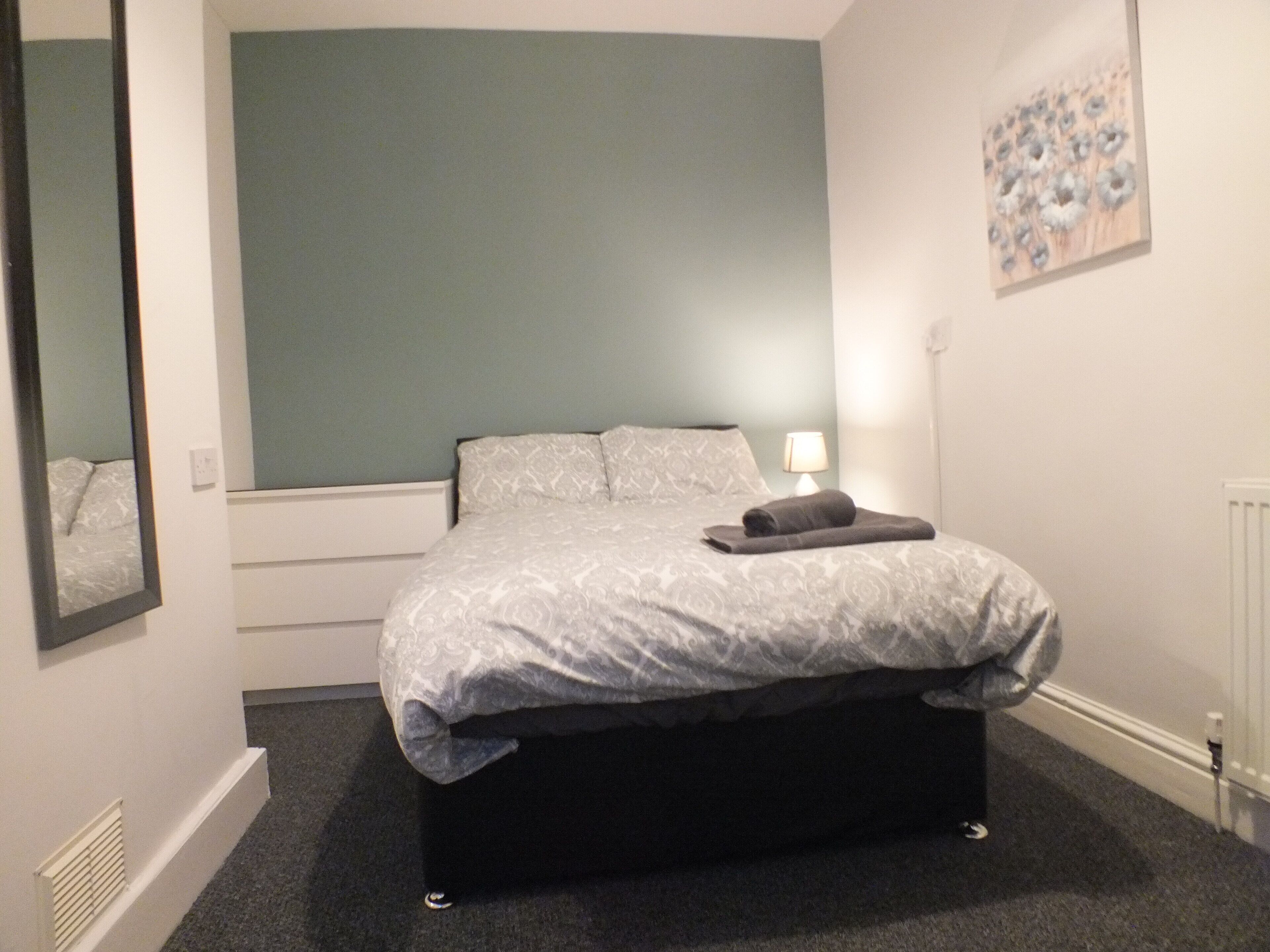 A bedroom with a bed, a nightstand, a lamp, and a painting on the wall.