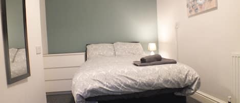 A bedroom with a bed, a nightstand, a lamp, and a painting on the wall.