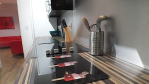 A kitchen with a black countertop, a red sofa in the background, and a wall-mounted TV. - Walthall Place (Crewe)