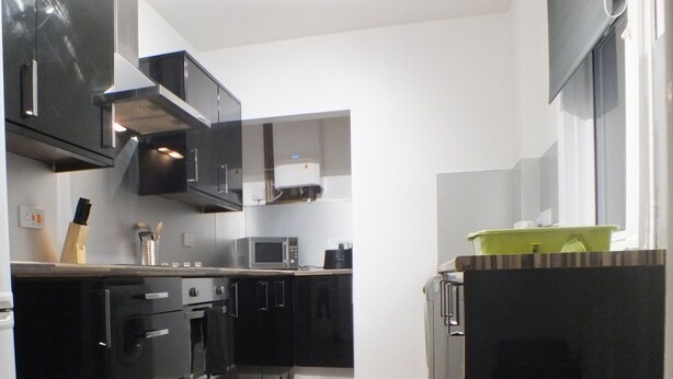 A modern kitchen with black cabinetry, a microwave, and a built-in oven. - Walthall Place (Crewe)
