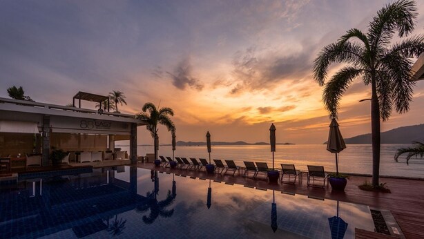 A poolside area with lounge chairs and umbrellas, overlooking a body of water during sunset. - Serenity Grand Seaview Suite (Rawai)