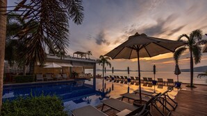 A poolside area with lounge chairs and umbrellas, overlooking a body of water at sunset. - Serenity Grand Seaview Suite (Rawai)