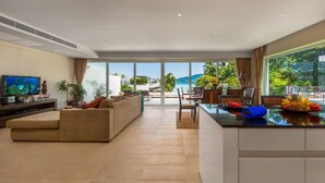 A spacious living room with a large sofa, a dining area with a table and chairs, a kitchen with a fruit bowl, and a TV. - Serenity Grand Seaview Suite (Rawai)