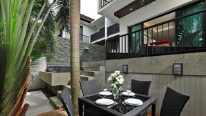 Un espace de restauration extérieur moderne, agrémenté d’un mur en pierre, de mobilier en rotin noir et d’une plante tropicale.