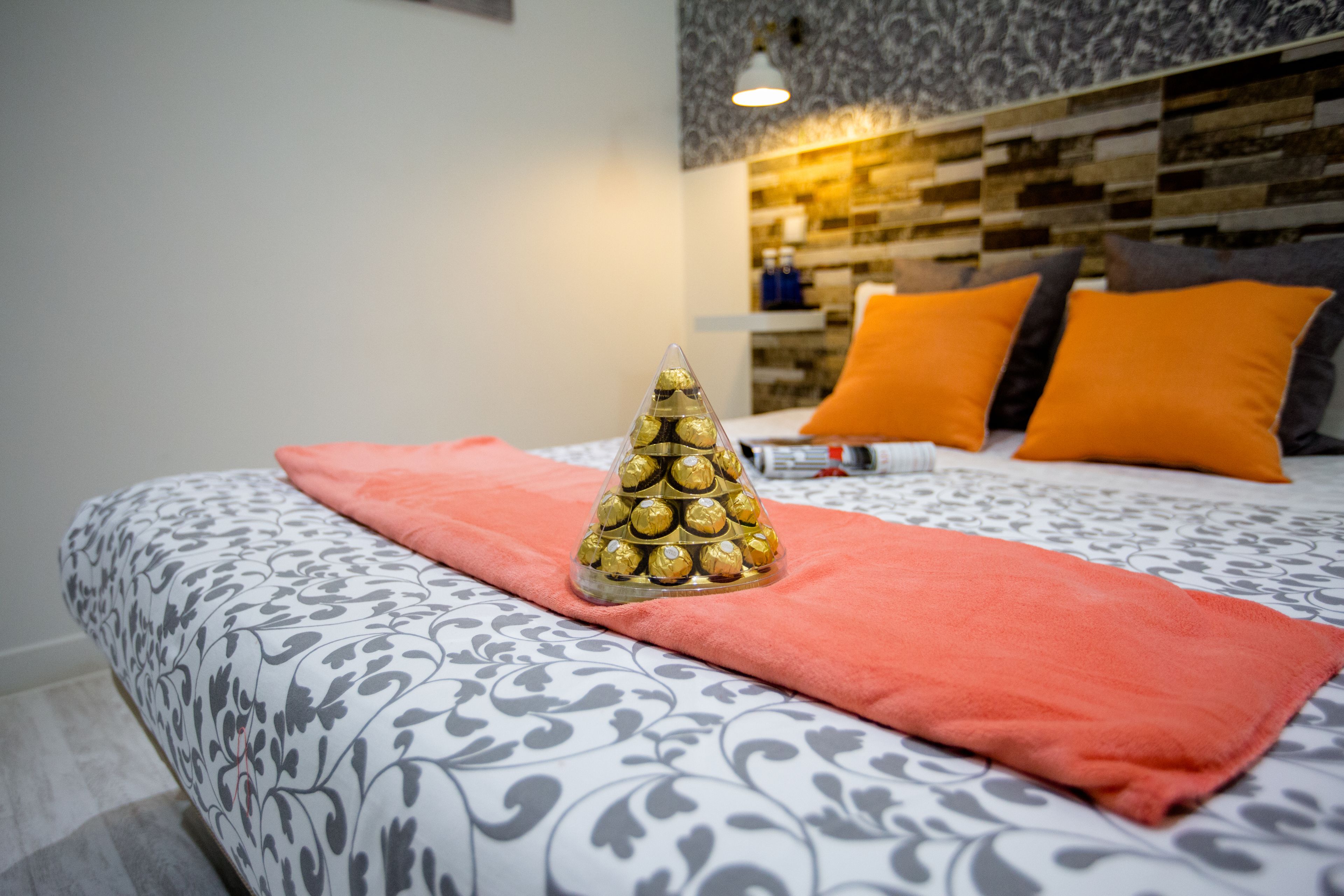 A neatly made bed with a patterned bedspread, a decorative golden cone, and a red towel.