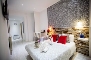 Una camera d'hotel moderna con un letto grande, una piccola scrivania, una TV fissata al muro e una parete decorata con un motivo a disegno.