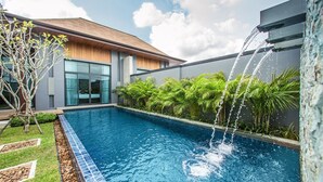 Een modern zwembad met een waterval, omringd door weelderige beplanting en een eigentijds gebouw.