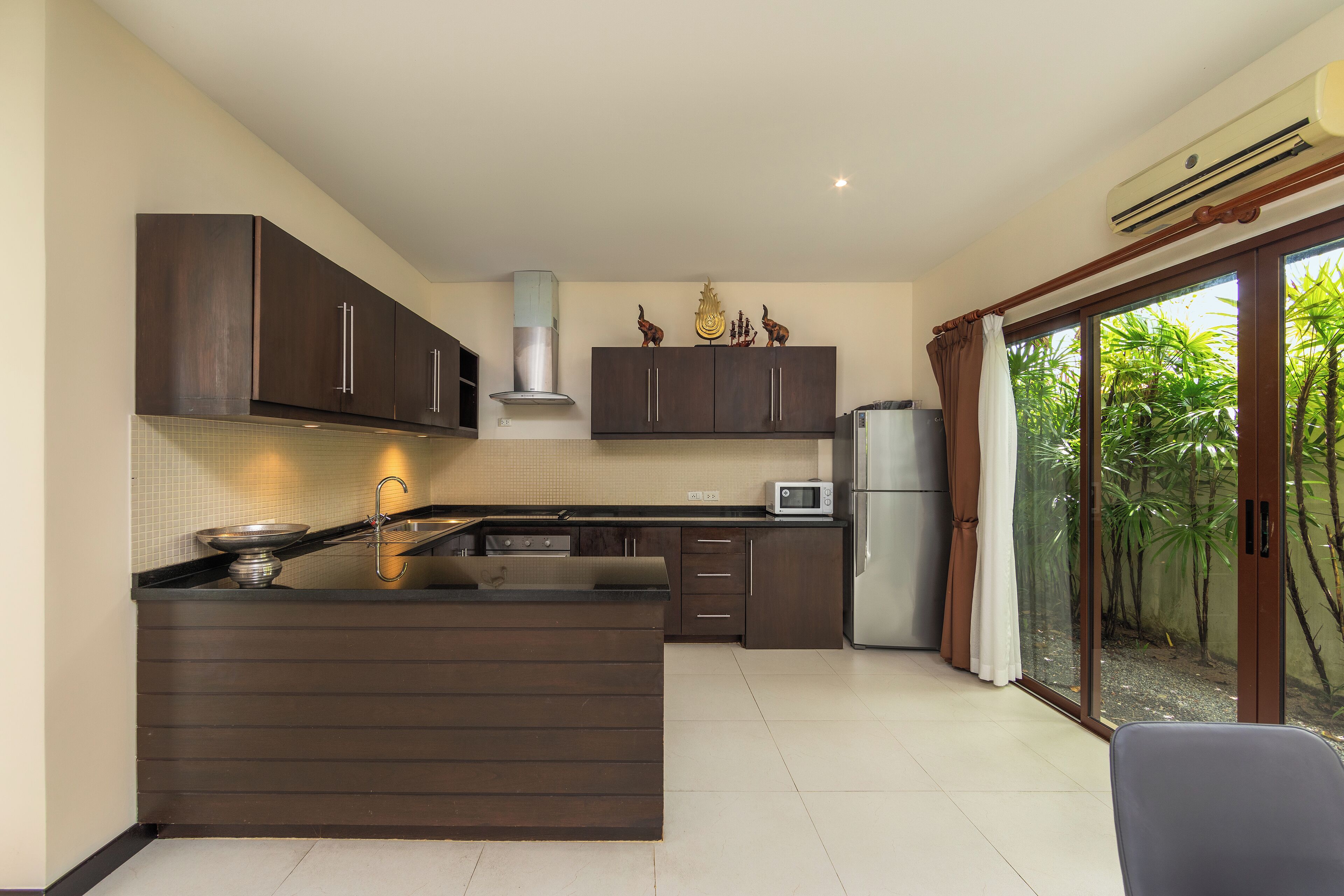 A modern kitchen with dark wood cabinets, a central island, and a view of greenery through a sliding glass door.