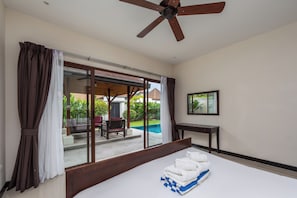 A bedroom with a bed, a ceiling fan, a window with curtains, and a view of an outdoor area with a pool and furniture. - Villa Iorangi (Rawai)