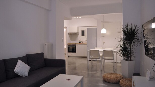 Un salon moderne avec un canapé foncé, une table basse blanche et un coin repas comprenant des chaises blanches et une petite table.