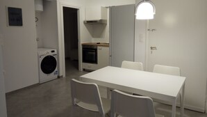 Une cuisine compacte équipée d’un lave-linge, d’une table à manger avec des chaises et d’un luminaire suspendu qui apporte de la lumière.