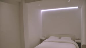 Une chambre à coucher au style minimaliste, avec un lit simple, des tables de chevet et un éclairage encastré au plafond.