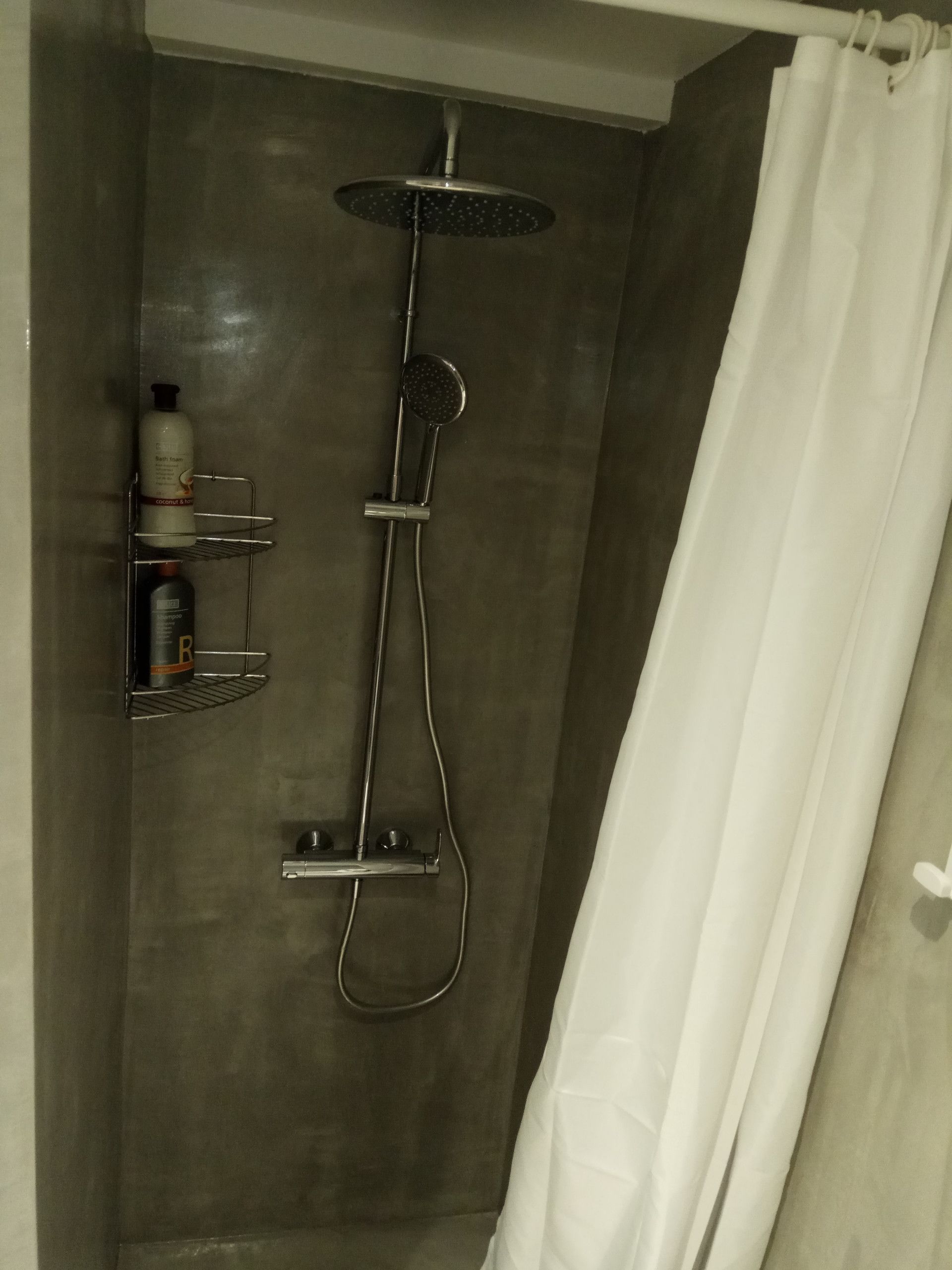 A shower area with a handheld showerhead, a wall-mounted faucet, and a shelf with toiletries.