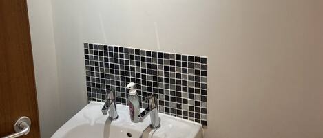 A bathroom with a white sink, a mirror above it, and black tiled backsplash.