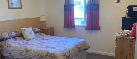 A bedroom with a bed, a chandelier, a window with curtains, a desk with a computer, and a deer head decoration.