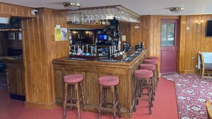 A bar area with wooden paneling, a cashless payment sign, multiple beer taps, and red bar stools. - The Jolly Drayman Pub and Hotel (Gravesend)