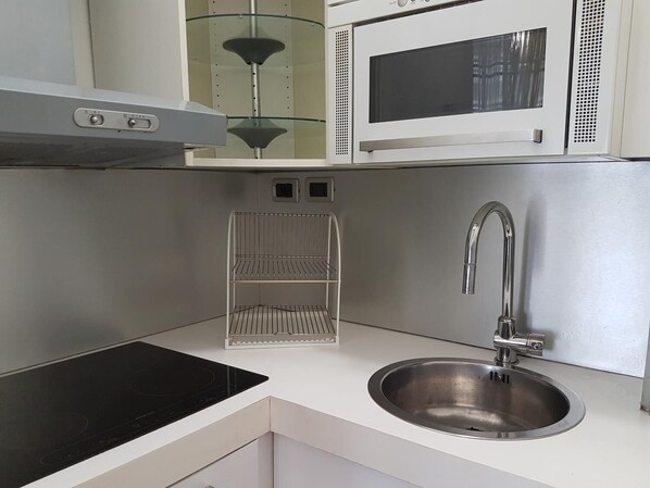 A compact kitchen with a stainless steel sink, a microwave, and a glass shelf unit. - Sant'Ambrogio Flat (Milan)