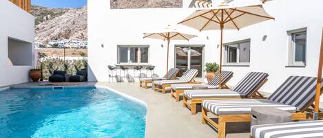 Un espace aménagé au bord de la piscine, avec des chaises longues et des parasols, une piscine, et une vue sur un paysage montagneux.