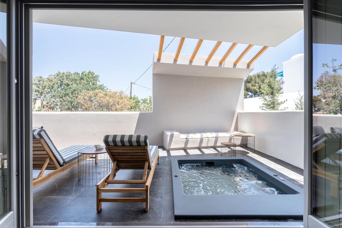 A rooftop terrace with a hot tub, wooden lounge chairs, and a small table.