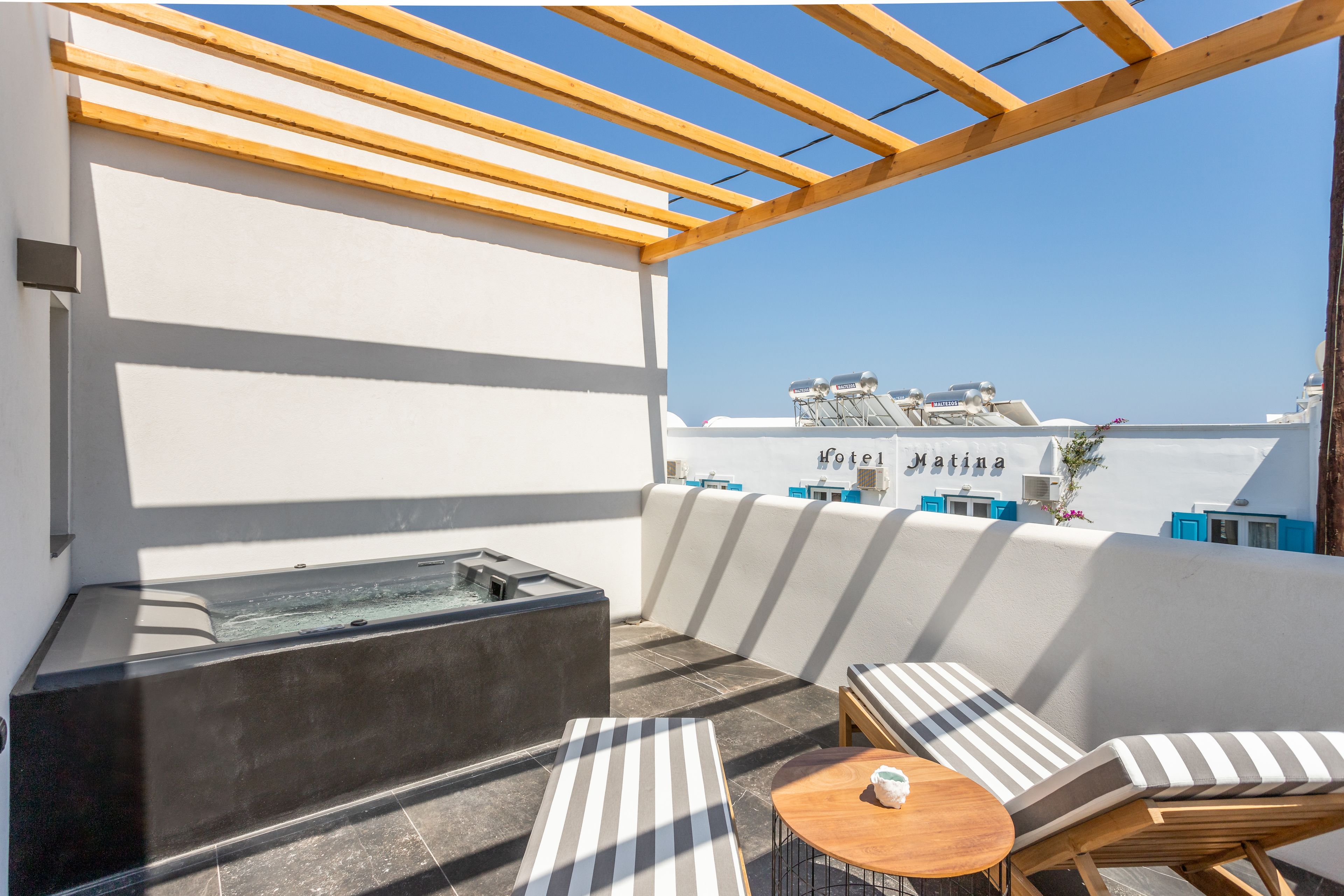 Una terraza en la azotea con un jacuzzi, cojines a rayas y una pequeña mesa redonda.