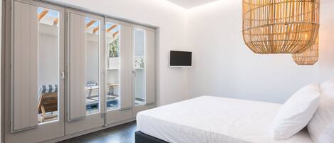 Un dormitorio moderno con una cama grande, un televisor y un ventanal corredero que da a un balcón.