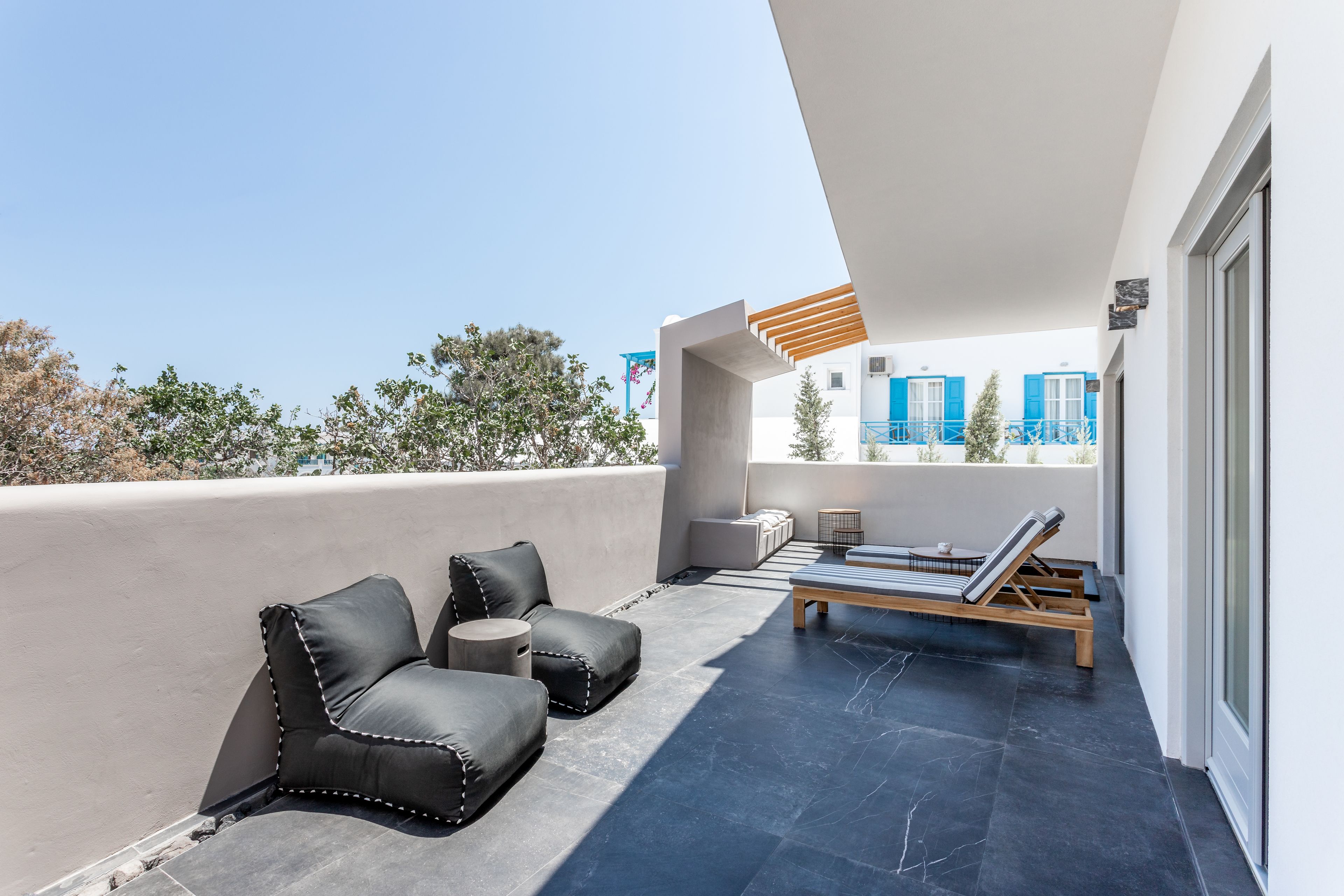 A rooftop terrace with black leather sofas, a wooden lounge chair, and a small round table.