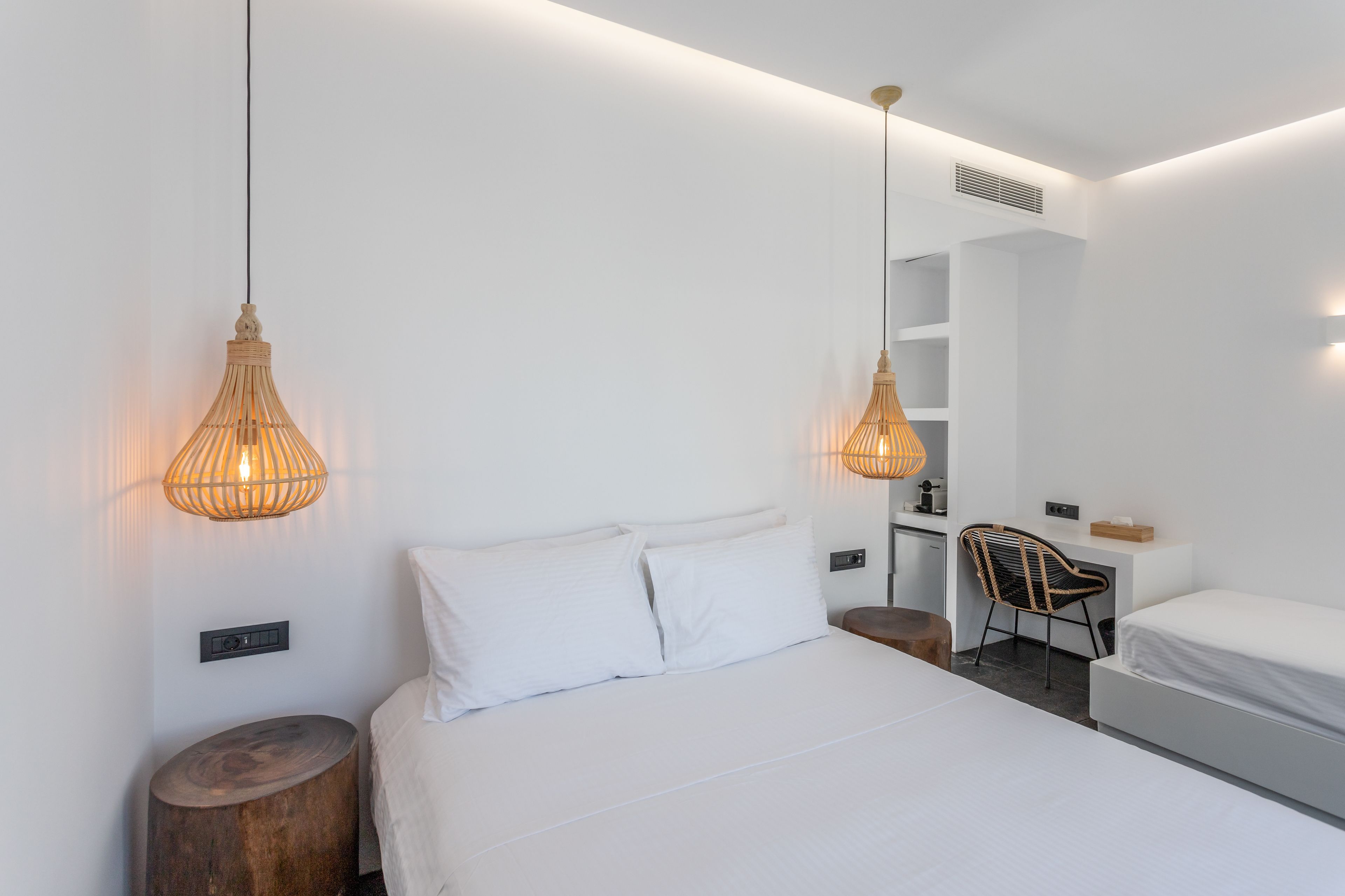 A modern hotel room with a large bed, two wall-mounted lamps, a wooden side table, a small desk with a chair, and a mirror on the wall.
