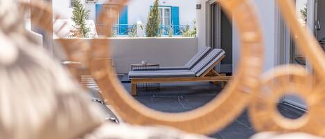 A sun lounger on a balcony with a view of a building with blue shutters.