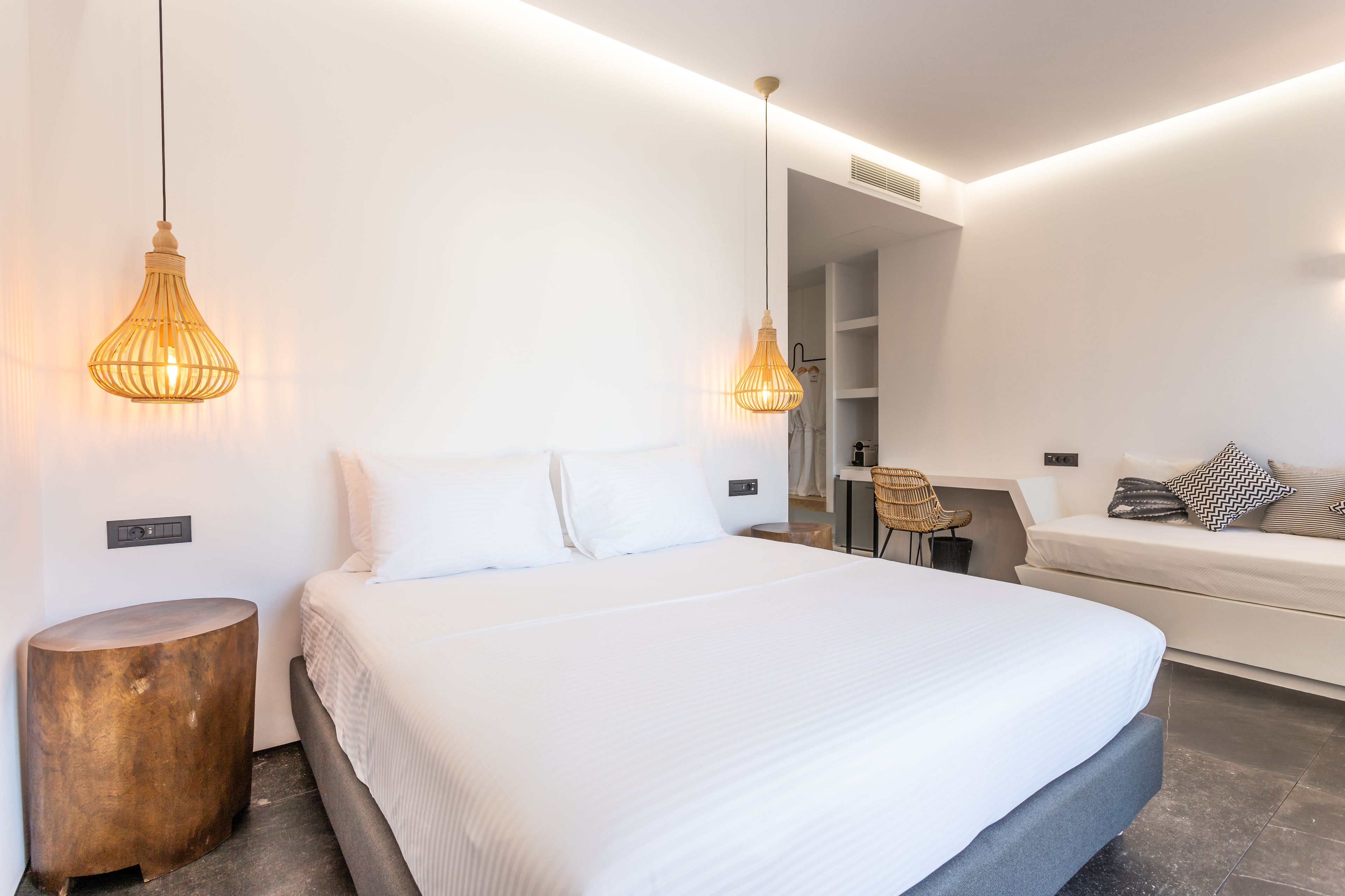 A modern bedroom with a large bed, bedside tables, a seating area with a chair, and pendant lighting.
